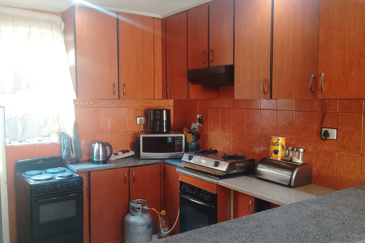 A functional kitchen featuring wood-look cabinetry, granite countertops, a breakfast bar, and tiled backsplash, offering a practical layout for daily meal preparation.