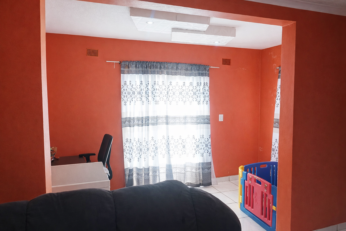 A living area featuring tiled flooring and recessed ceiling lighting, currently utilized as a multi-purpose space with bright orange wall finishes.
