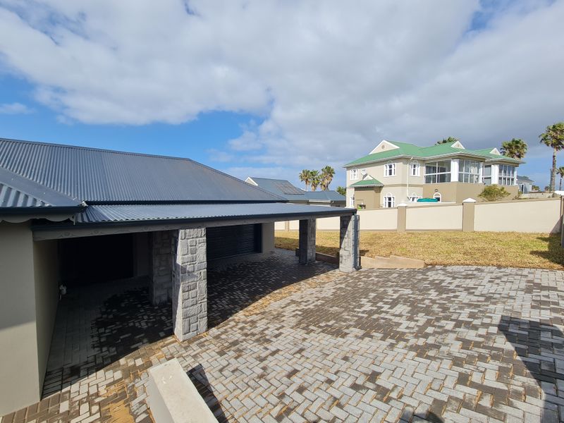 Front exterior view featuring a double garage with a corrugated metal roof, stone-clad pillars, and a paved driveway.