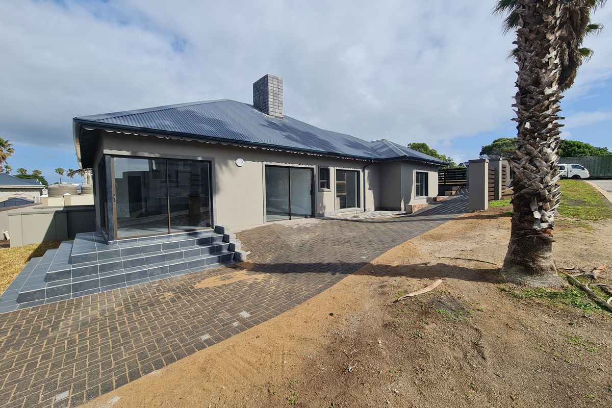 Rear exterior view of the house featuring a tiled patio, sliding glass doors, and a paved driveway area with surrounding unfinished landscaping.