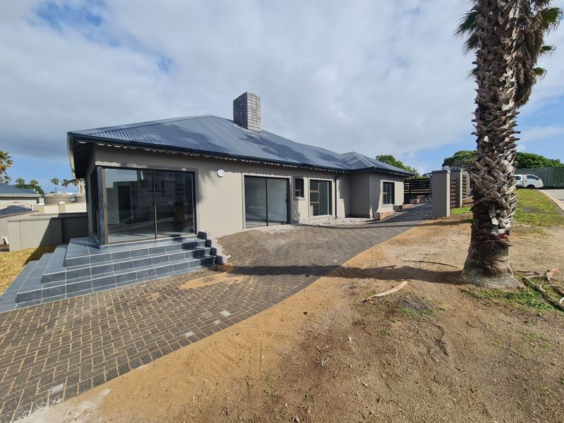 Rear exterior view of the house featuring a tiled patio, sliding glass doors, and a paved driveway area with surrounding unfinished landscaping.