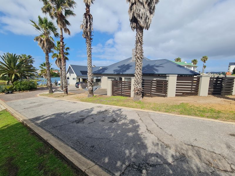 Front exterior view of a residential property featuring a corrugated metal roof, timber slat fencing, and a paved driveway with mature palm trees.
