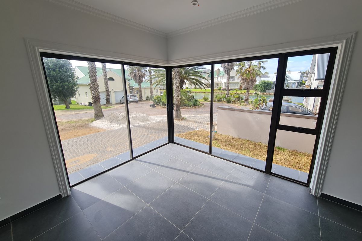 A bright, empty living space featuring large corner sliding glass doors that provide expansive views of the surrounding neighbourhood and garden.