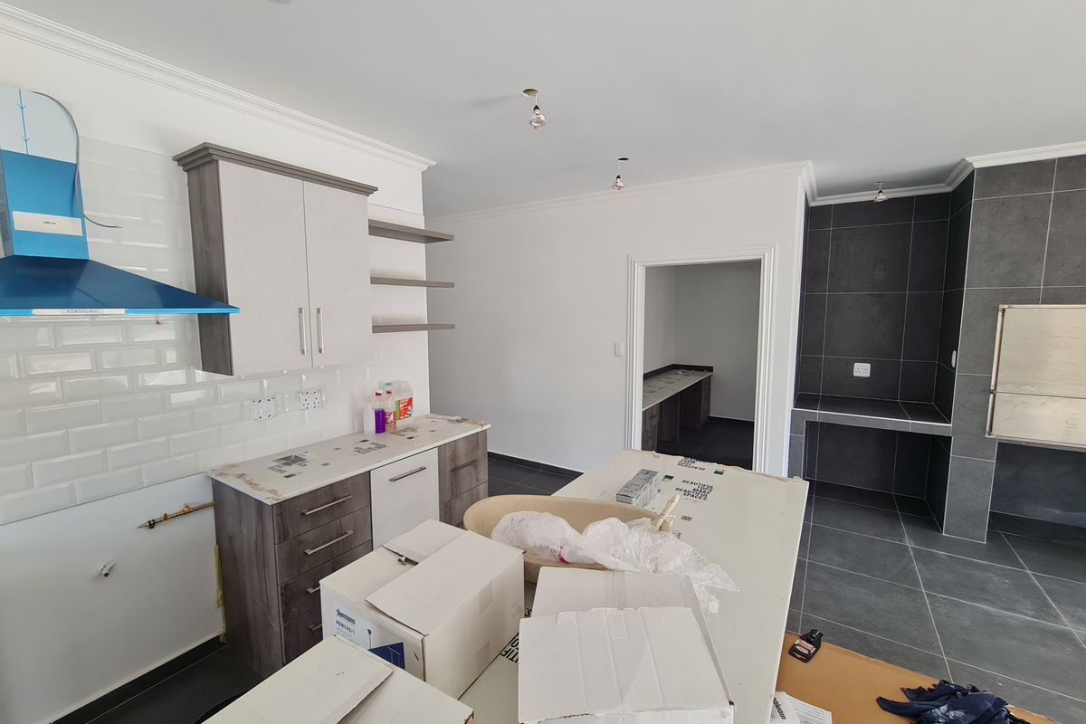Modern kitchen featuring sleek cabinetry, subway tile backsplash, stone countertops, and a built-in braai area, currently undergoing final finishing touches.