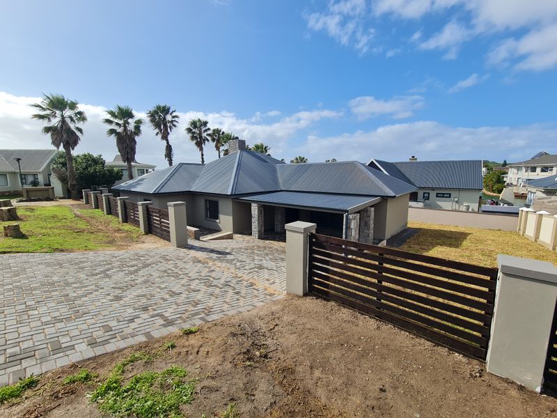 Front elevation of a modern house featuring a paved driveway, timber slat fencing, stone cladding accents, and a metal roof.