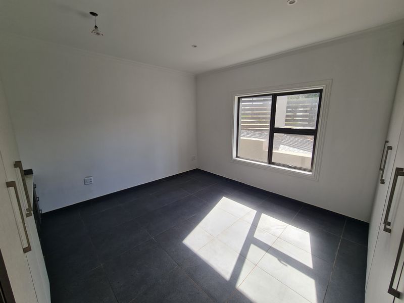 A bright, empty bedroom featuring modern dark floor tiles, built-in cupboards, and neutral white walls, ready for personalization.