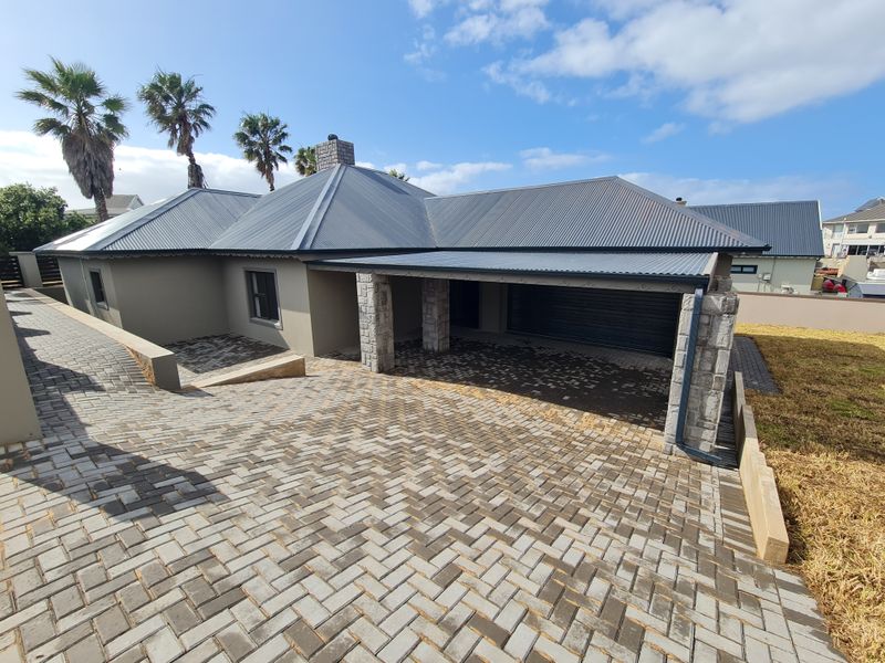 Front elevation of a modern house featuring a corrugated metal roof, stone-clad pillars, and an extensive paved driveway leading to the garage.