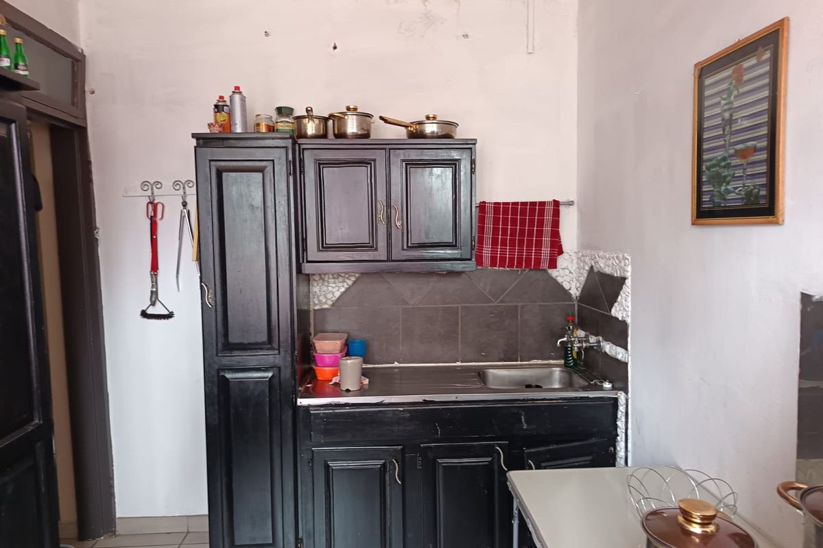 A compact kitchen area featuring dark built-in cabinetry, a stainless steel sink, and a tiled splashback, requiring cosmetic updates to the surrounding wall finishes.