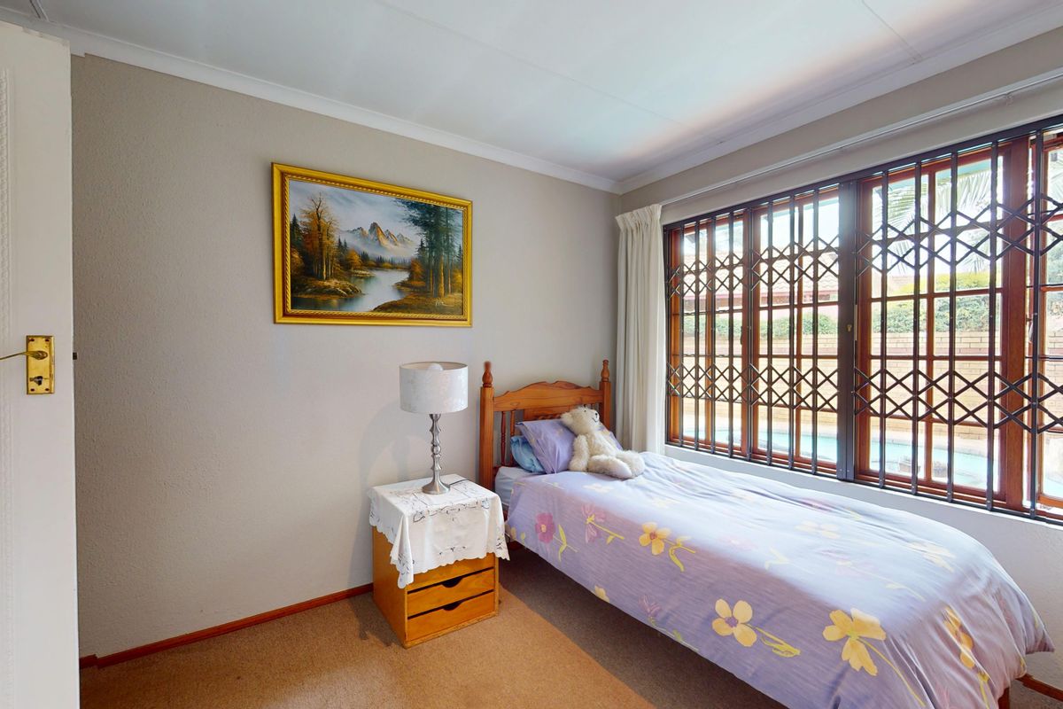 A bedroom featuring neutral wall tones, carpeted flooring, and a large window fitted with a metal security gate.