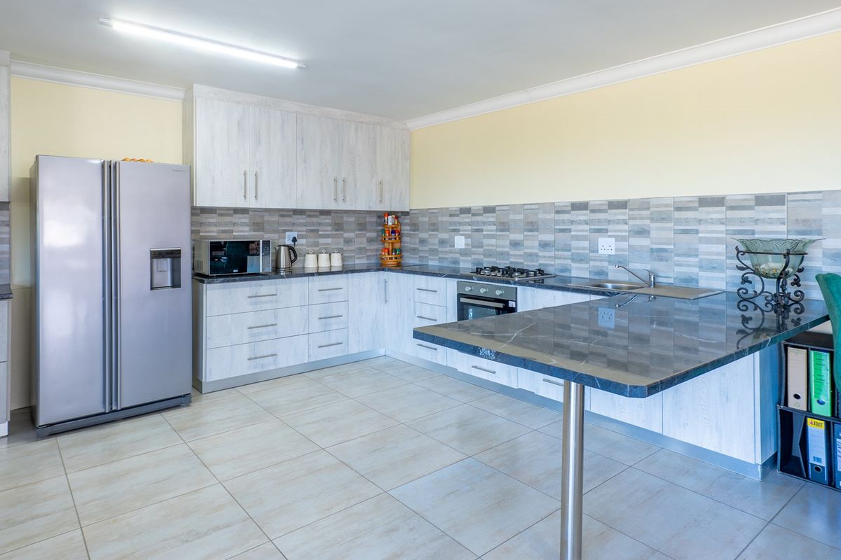 Modern kitchen featuring light wood-grain cabinetry, dark stone countertops, a breakfast bar, and a tiled backsplash with integrated gas hob and oven.