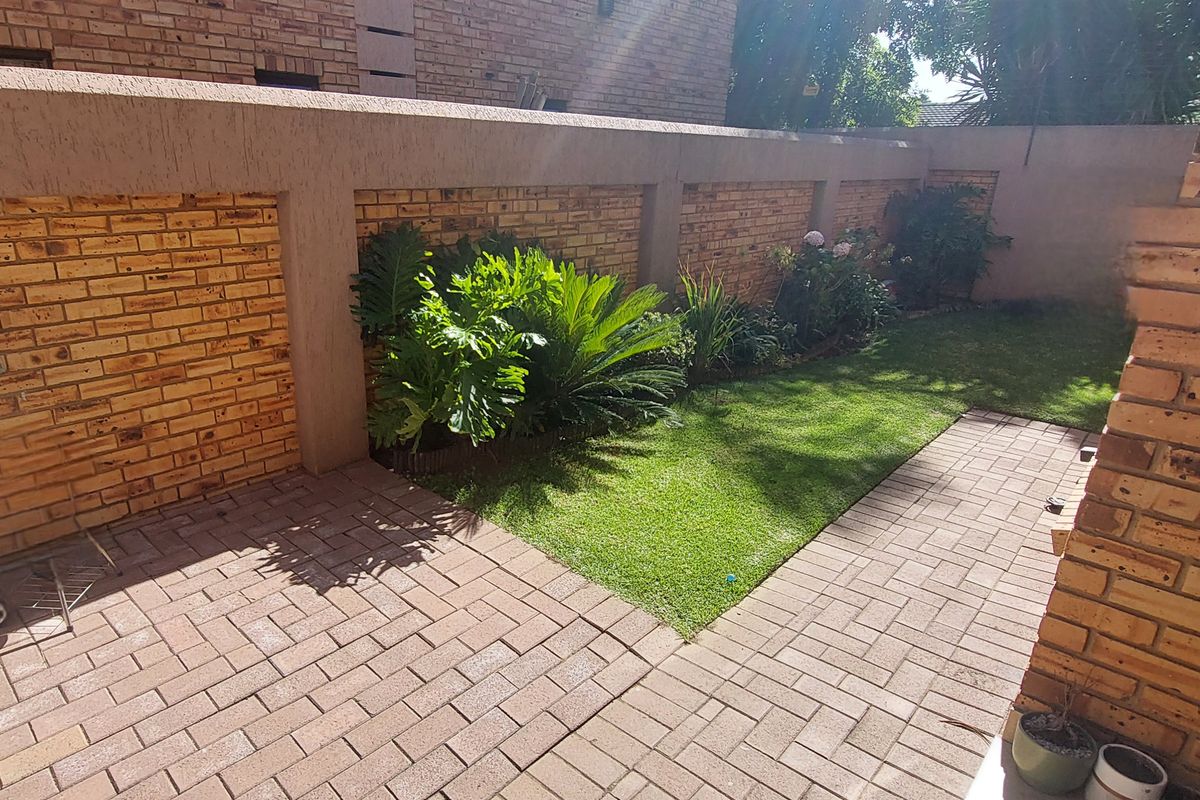 A private rear courtyard featuring a paved patio area, a small lawn, and established perimeter brick boundary walls.