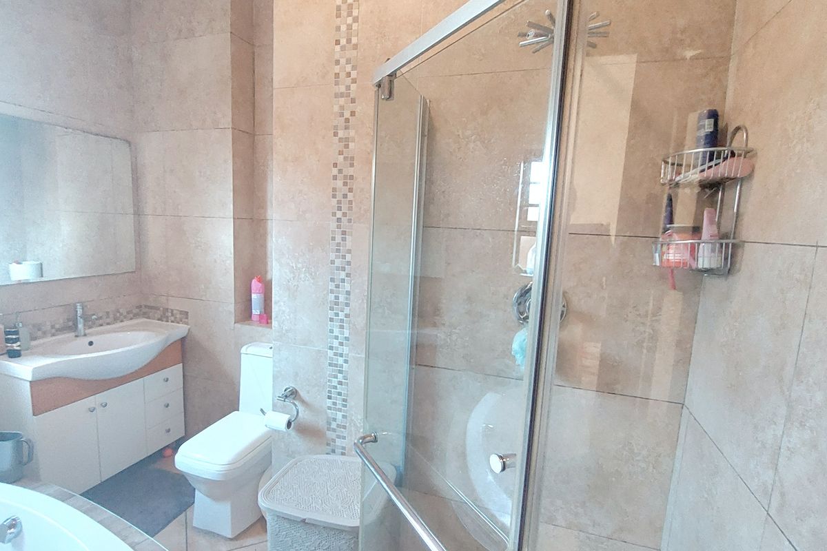 A functional bathroom featuring a vanity with basin, a toilet, a glass-enclosed shower, and a built-in bathtub with neutral wall and floor tiling.