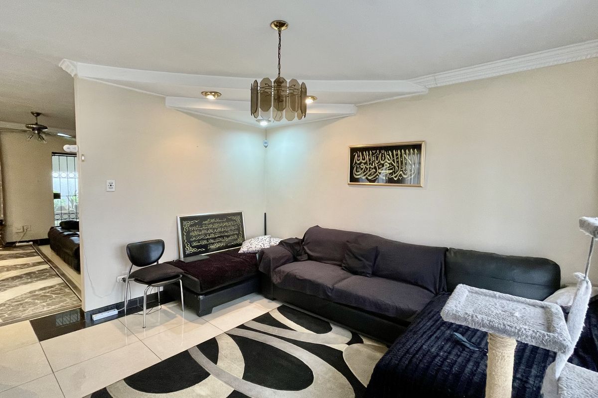 A living room area featuring tiled flooring, decorative ceiling molding, and a central pendant light fixture, with an open-plan layout leading to an adjacent space.