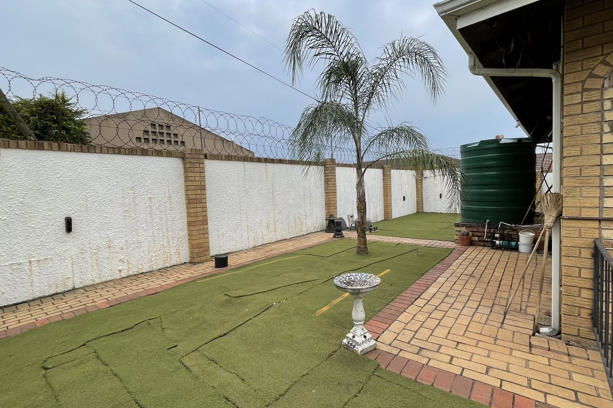 A rear garden area featuring a brick-walled perimeter with security fencing, artificial turf, and a water storage tank.