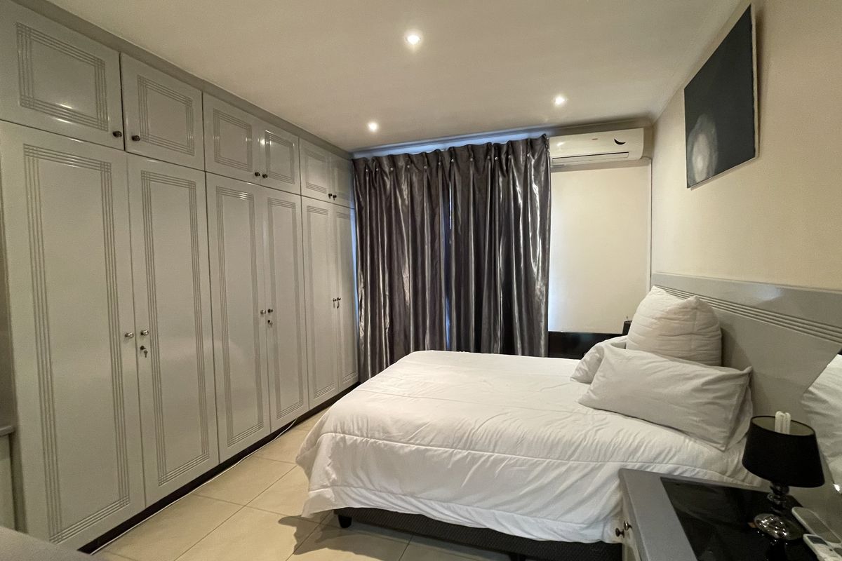 A well-maintained bedroom featuring extensive floor-to-ceiling built-in cabinetry, tiled flooring, and a wall-mounted air conditioning unit.