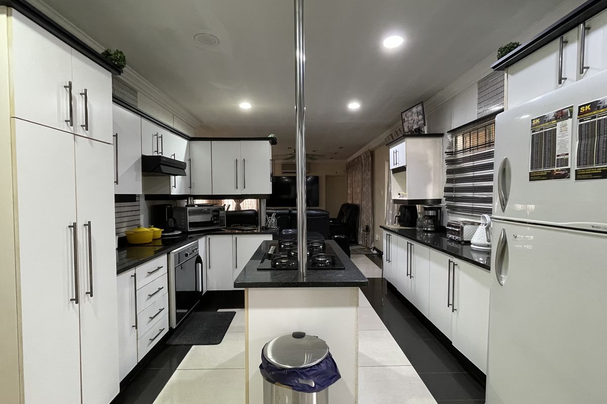 Modern kitchen featuring white cabinetry, black countertops, a central island with a built-in gas hob, and recessed ceiling lighting.