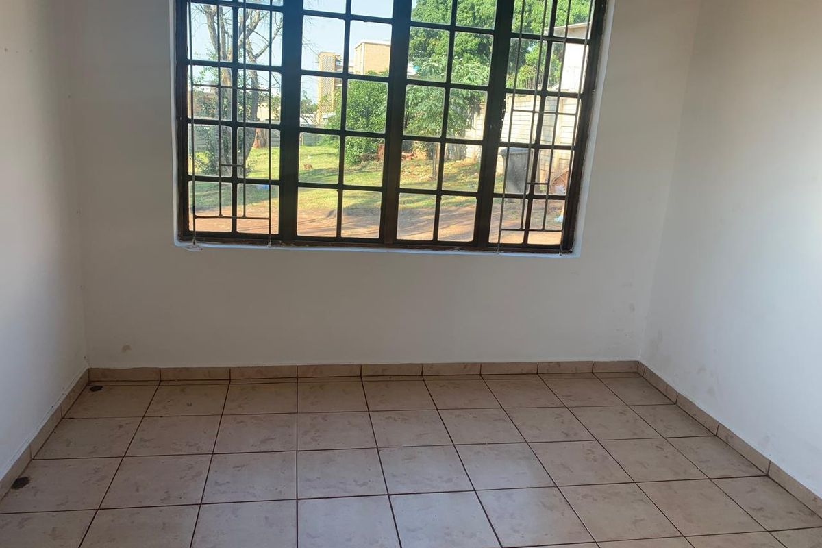 An empty bedroom featuring tiled flooring and a large steel-framed window, providing a blank canvas for potential interior design updates.