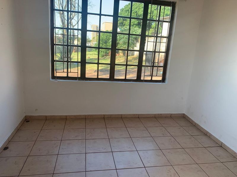 An empty bedroom featuring tiled flooring and a large steel-framed window, providing a blank canvas for potential interior design updates.