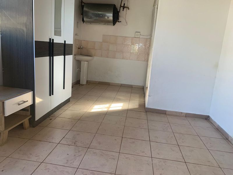 A utility space featuring a pedestal sink, tiled splashback, and an electric water heater, with ceramic floor tiles throughout.