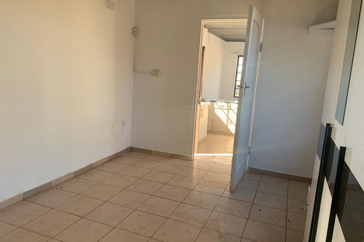 An empty bedroom featuring tiled flooring and a built-in cupboard, with a doorway leading through to the kitchen area.