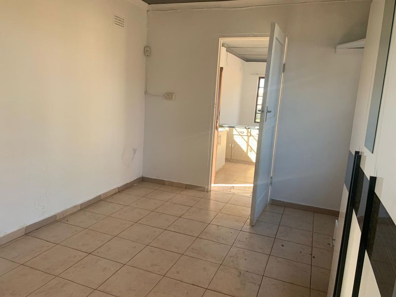 An empty bedroom featuring tiled flooring and a built-in cupboard, with a doorway leading through to the kitchen area.