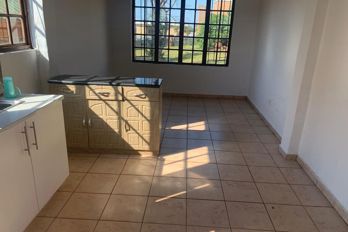 An empty kitchen area featuring tiled flooring, built-in cabinetry with granite countertops, and windows fitted with security bars.