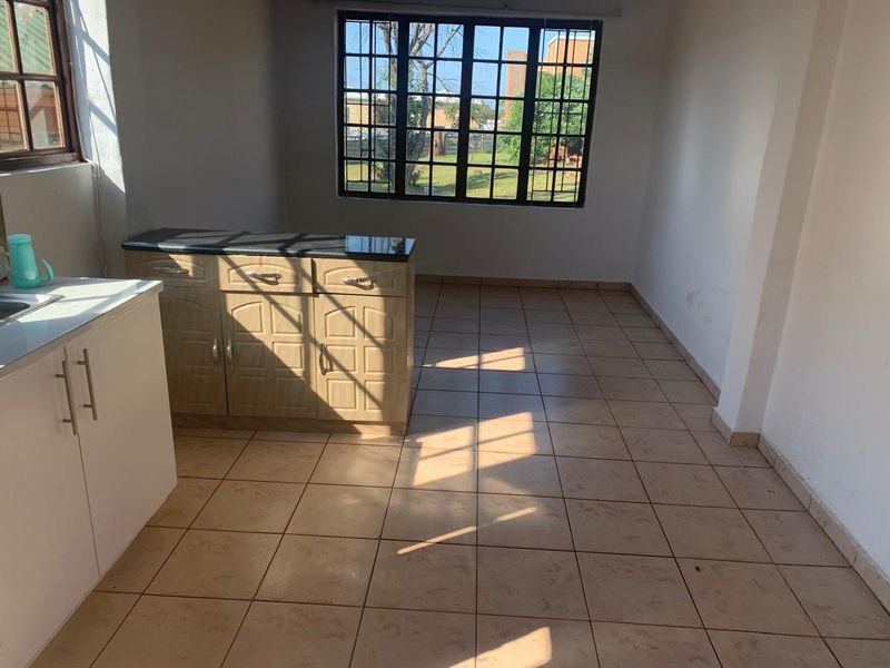 An empty kitchen area featuring tiled flooring, built-in cabinetry with granite countertops, and windows fitted with security bars.