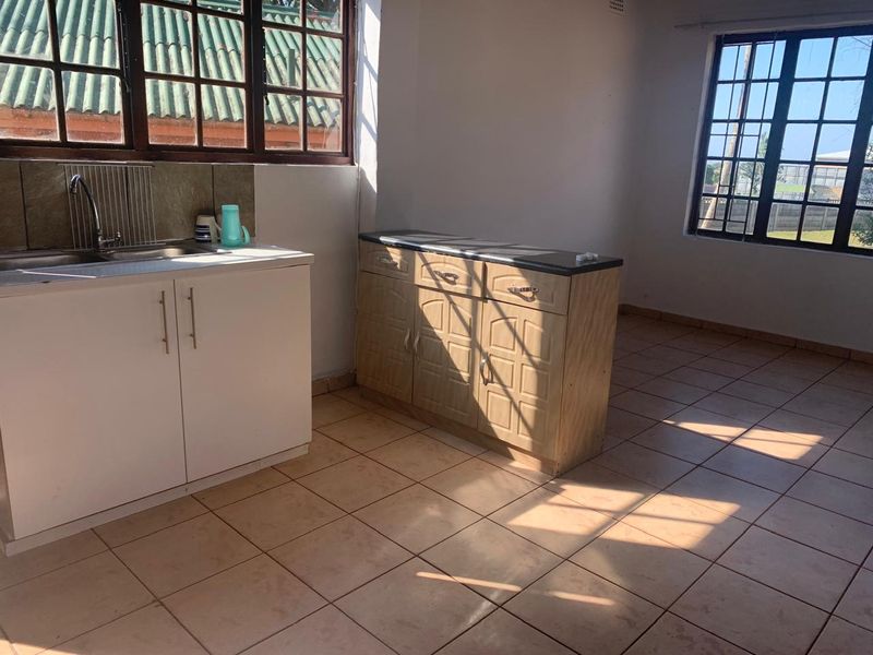 A functional kitchen area featuring tiled flooring, built-in cabinetry, and a stainless steel sink, illuminated by natural light from large grid-style windows.