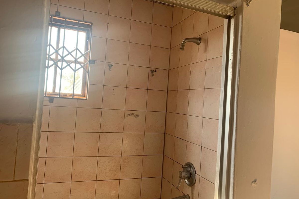 A dated bathroom shower area featuring original wall tiles, a shower mixer, and a window with a security gate.