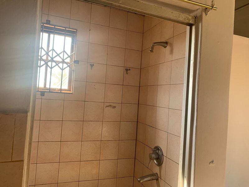 A dated bathroom shower area featuring original wall tiles, a shower mixer, and a window with a security gate.