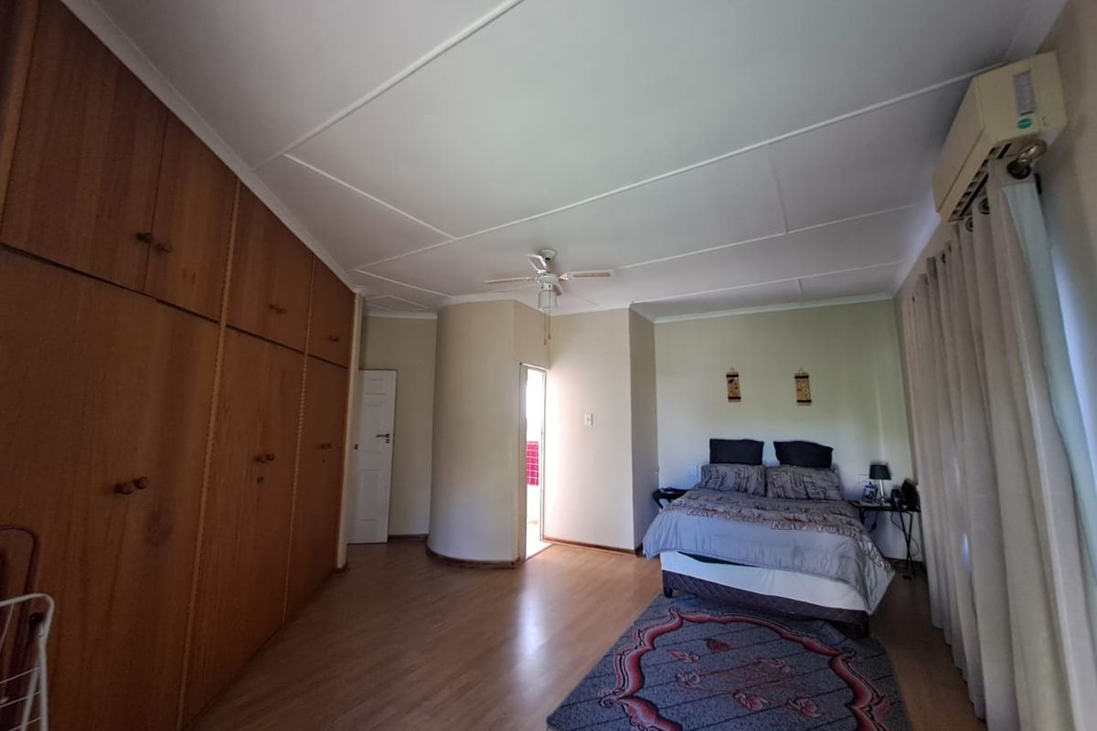 Spacious bedroom featuring extensive built-in wooden cabinetry, laminate flooring, a ceiling fan, and a wall-mounted air conditioning unit.
