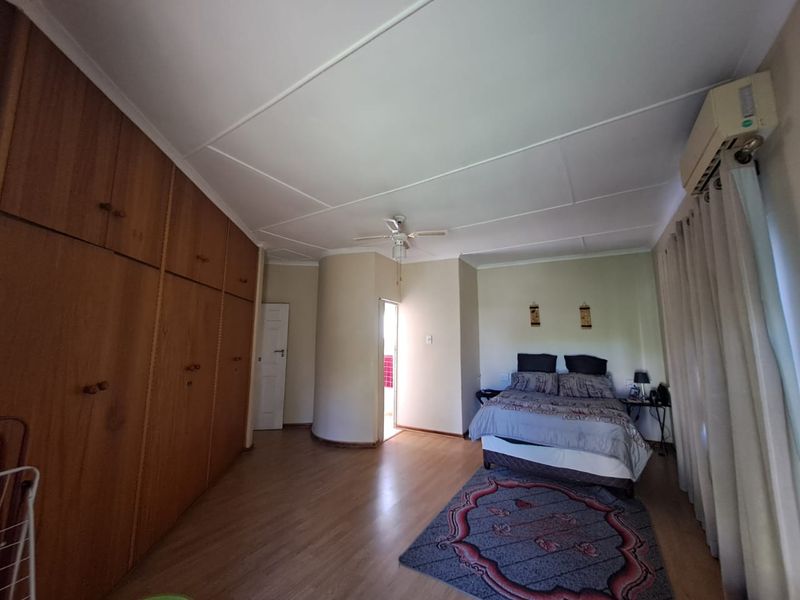 Spacious bedroom featuring extensive built-in wooden cabinetry, laminate flooring, a ceiling fan, and a wall-mounted air conditioning unit.