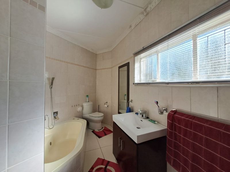 A functional bathroom featuring a built-in bathtub, toilet, and vanity cabinet with a washbasin, finished with neutral wall and floor tiles.