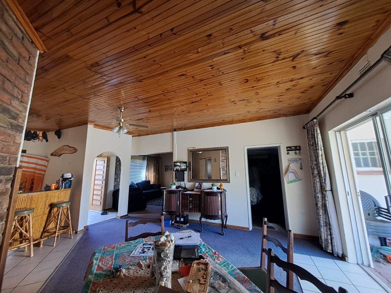 Open plan living and dining area featuring a distinctive timber tongue and groove ceiling, brick accent wall, and direct access to the outdoor patio.