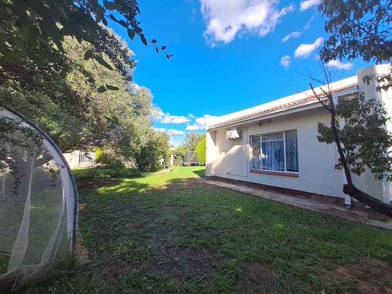 A view of the rear garden and the back elevation of the house, featuring a lawn area and exterior wall mounted air conditioning unit.