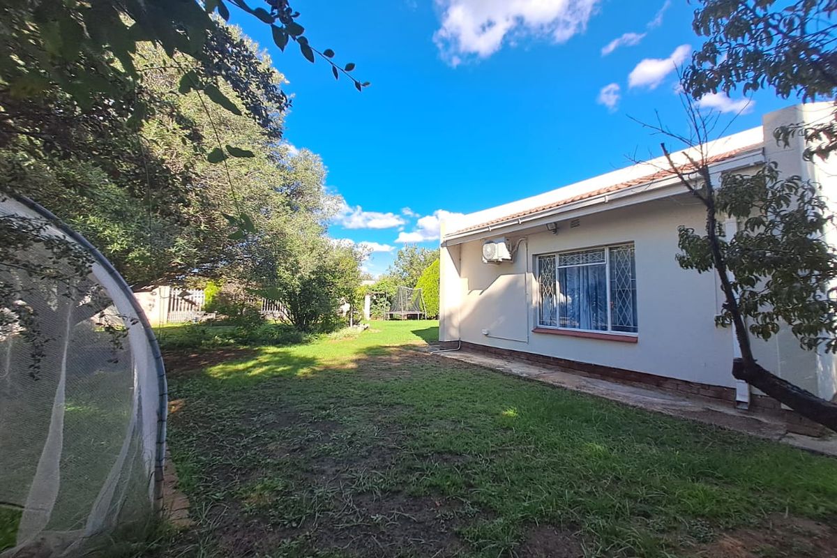 A view of the rear garden and the back elevation of the house, featuring a lawn area and exterior wall mounted air conditioning unit.