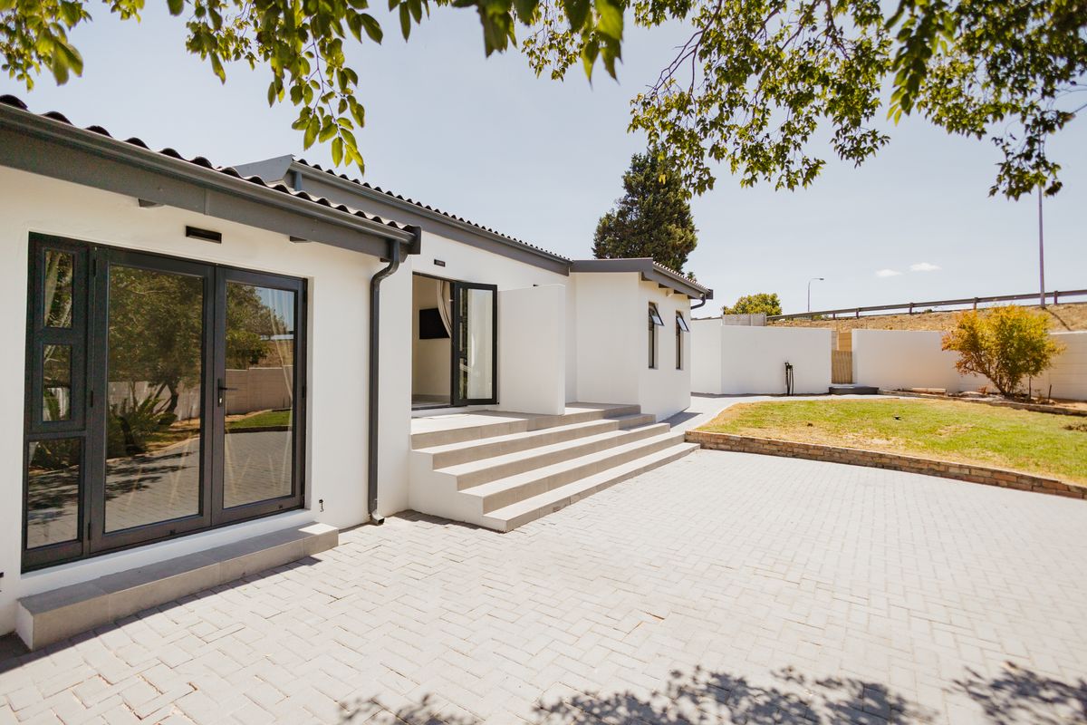 Rear view of the property featuring a paved patio area, concrete steps leading to glass doors, and a well-maintained exterior facade.