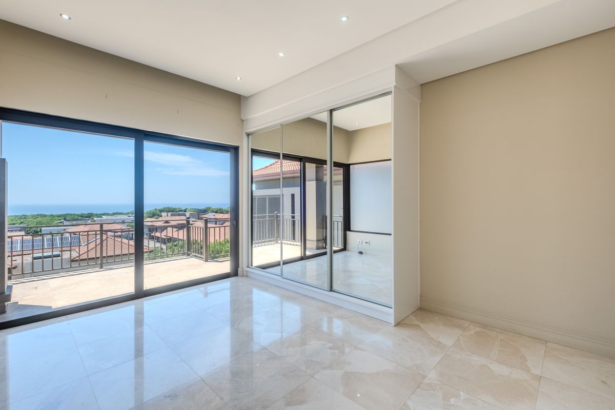 Spacious bedroom featuring polished tile flooring, large mirrored built-in cupboards, and sliding glass doors opening onto a balcony with scenic coastal views.