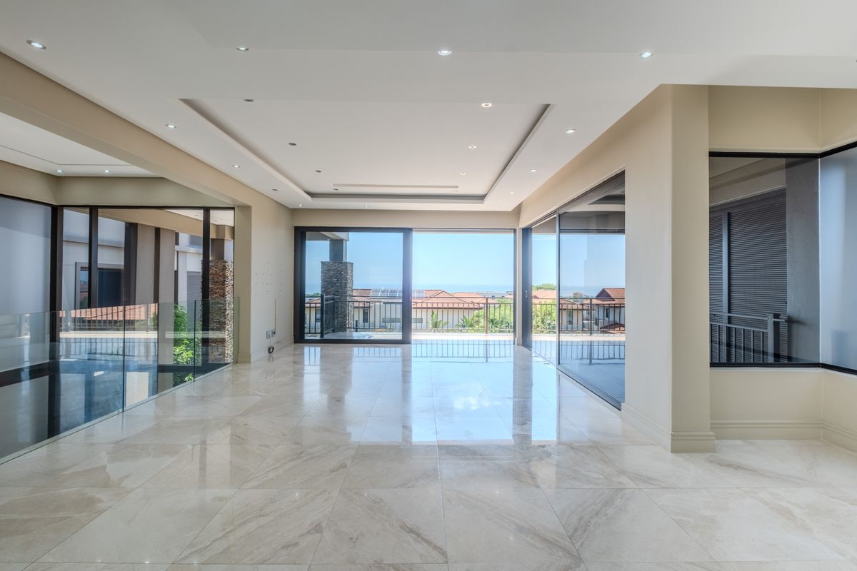 Spacious, light-filled living area featuring large format polished floor tiles, recessed ceiling lighting, and expansive sliding glass doors opening to a balcony with views.