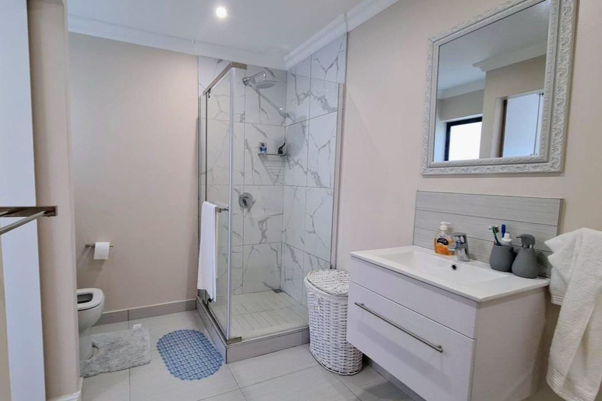 A modern bathroom featuring a glass-enclosed shower with marble-look wall tiles, a contemporary vanity with a basin, and a wall-mounted mirror.