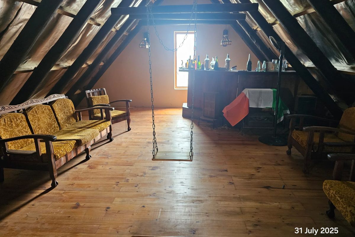 Attic space featuring exposed timber roof beams, wooden flooring, and a built-in bar area, offering potential for a unique living or entertainment room.