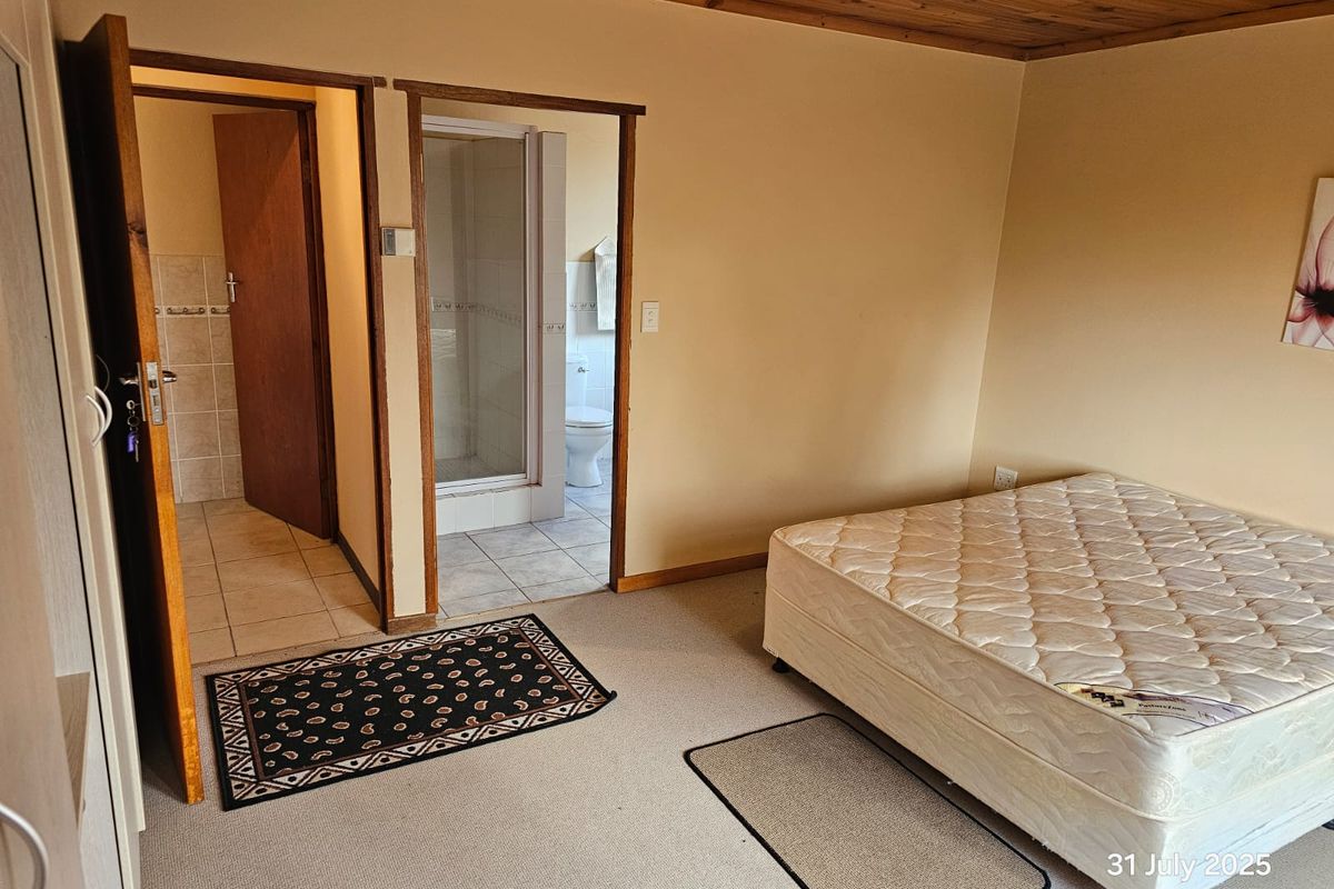 A bedroom featuring carpeted flooring, a timber ceiling, and an en-suite bathroom with a shower and toilet.