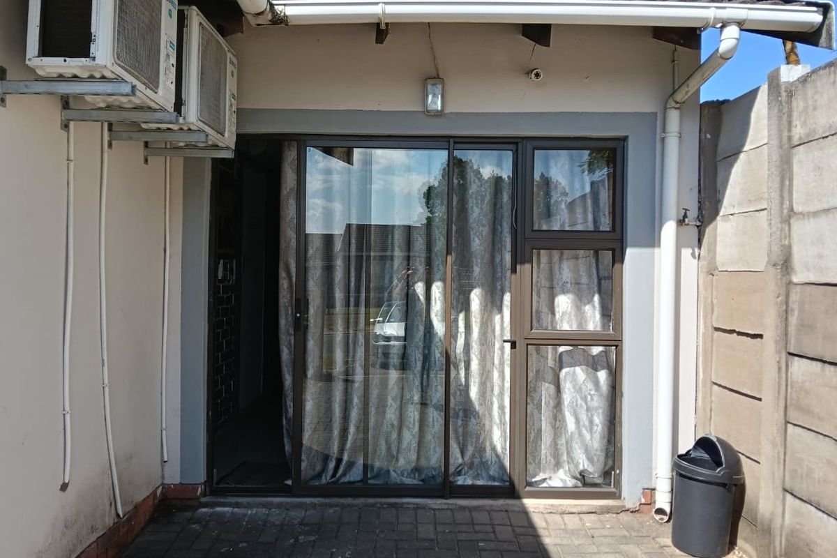 Rear exterior view of the apartment featuring a paved patio area, sliding glass door access, and wall-mounted air conditioning units.