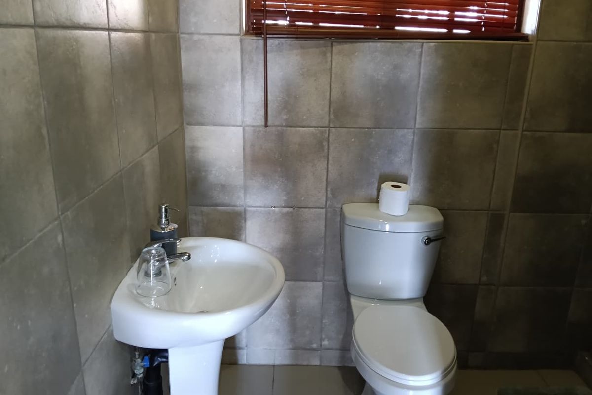 A compact bathroom featuring a pedestal basin, toilet, and neutral wall tiling with a window fitted with venetian blinds.