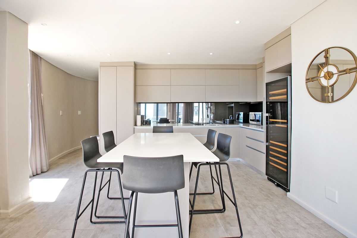 Modern kitchen featuring sleek handleless cabinetry, integrated wine cooler, mirrored splashback, and a central island with stone countertop.