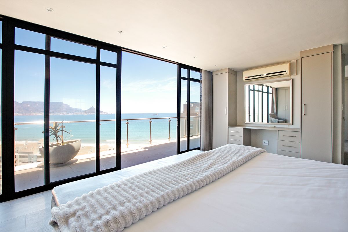 Modern bedroom featuring built-in cabinetry, a vanity, and large sliding doors opening onto a balcony with expansive ocean and mountain views.