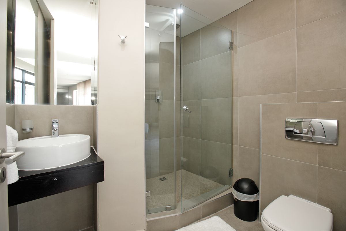 Modern bathroom featuring a vessel sink, wall-hung toilet with concealed cistern, and a glass-enclosed shower with neutral tiling.