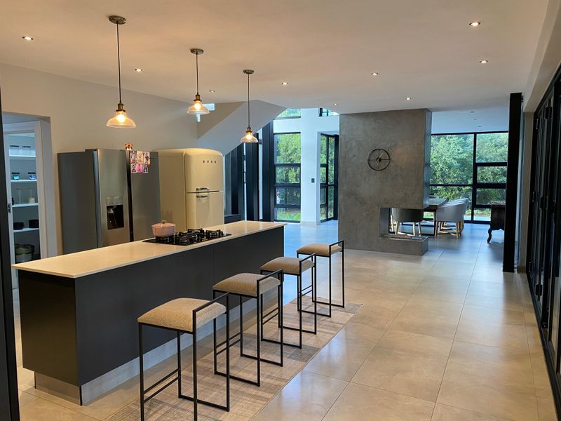 Modern open-plan living area featuring a sleek kitchen island with gas hob, tiled floors, and a striking double-sided concrete fireplace.