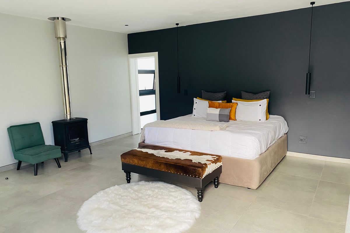 Spacious modern bedroom featuring large format floor tiles, a dark accent wall, and a built-in freestanding fireplace with a stainless steel flue.