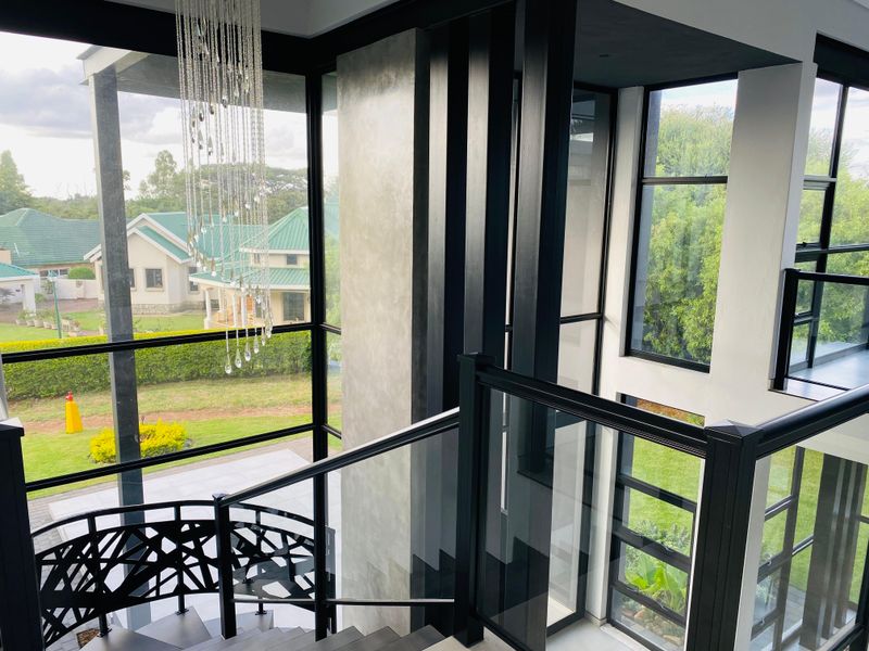 Modern double-volume hallway featuring a striking spiral staircase, glass balustrades, and expansive floor-to-ceiling windows offering scenic garden views.